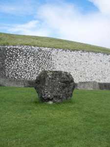 A large stone boulder in front of a massive mound of earth and stones.