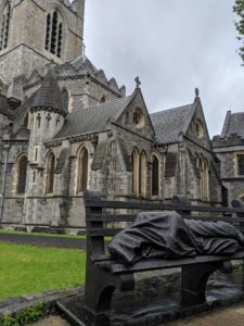 A statue of a person lying on a bench in front of Christ Church Cathedral in Dublin.