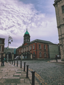 Historic Dublin street with cobblestones and a clock tower building under a cloudy sky