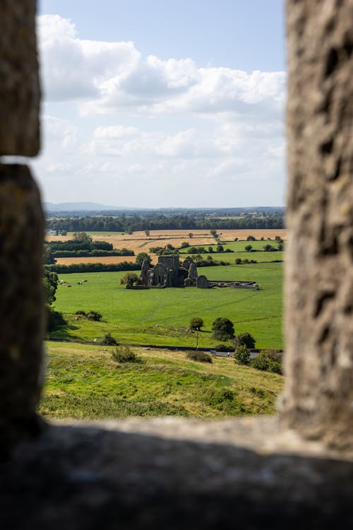 Ancient Irish ruins viewed through stone window overlooking green countryside fields