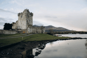 Medieval Irish castle beside calm lake with mountains in the background