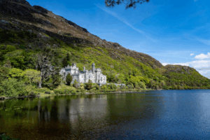 Historic Irish castle beside lake surrounded by green mountains and trees