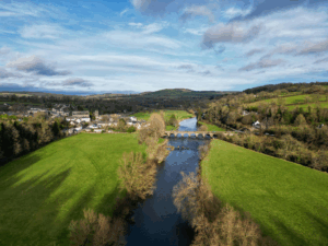This photo shows an aerial view of grass, a river, and some houses.