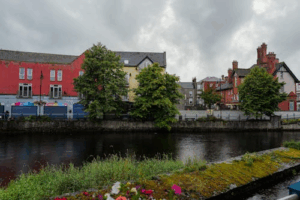Colorful buildings along a riverside in a traditional Irish town under cloudy skies