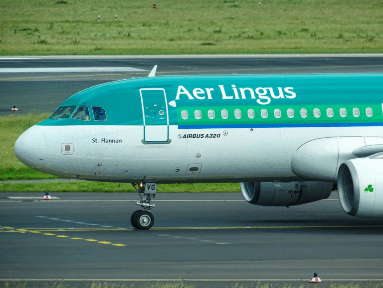 Green and white Aer Lingus airplane descending for landing over green landscapes.