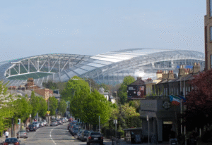 This image shows a modern stadium seen from a tree lined street.