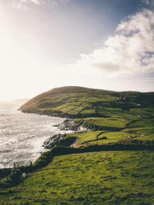 Aerial view of lush green coastal fields and dramatic sea cliffs along the Irish coastline.